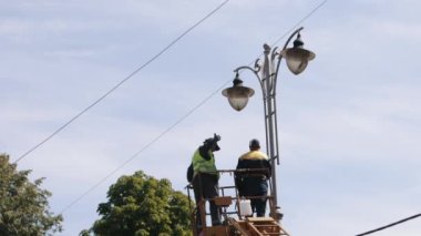 Municipal worker, repair street lamp, aerial device. Repair work at street light, worker fixing light pole lamp at height while wearing personal protective equipment, replacement of led lights