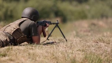In green uniform vest, a military man unloads a machine gun, a soldier lies with a gun, Army war concept, military, army gunner attacking, Corps Machine Gun Crew shooting, Army Gunner attacking.