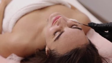 Plastik spatula, yüz kremi, kozmetoloji teknikleri. Kozmetik uzmanı plastik spatula kullanarak kadın hastaların yüzüne beyaz krem sürüyor..
