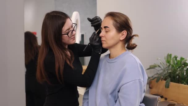永久の手順 眉メイク 顔のケア 若い女性が美容室で眉矯正手続きを受けている ブラウザのためのマイクロブレードの概念は 塗料が眉の色に使用されている — ストック動画