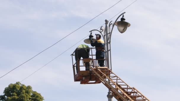 労働者の修理 街灯の技術者 高さの街路灯を修理する労働者 街灯柱の電球を交換する 個人的な保護を身に着けているリフトバケツの男性 — ストック動画