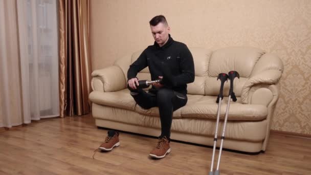 靴の装着 職業療法 彼の松葉杖が近くに横たわっている間 障害のために義足を使う男はソファに座って靴を履いています — ストック動画