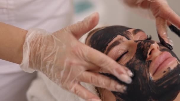 ブラックマスク ケープ若返り クレンジングトリートメント 美容室 スキンケアの専門家は 顔のデトックス リフティング 昆布若返り 泥療法を提供し クライアントの顔に黒いマスクを適用します — ストック動画