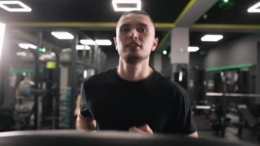 Koşu bandı, kardiyovasküler sağlık, koşu tekniği. Genç bir adamın portresi onu spor salonunda koşu bandında gösteriyor..
