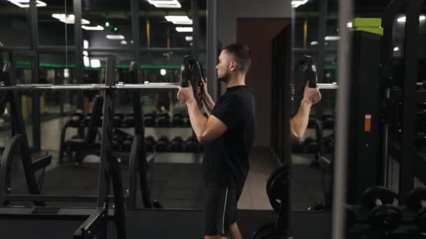 筋肉の構築 ジム機器 トレーニングプログラム 重量プレートは慎重にジムで男によってバーベルに追加されます — ストック動画