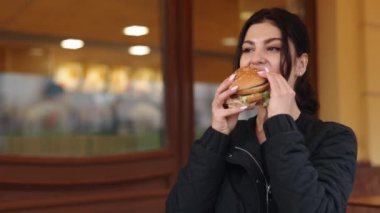 Restorana yakın, hamburgerci meraklısı, hamburgerci eğlencesi. Restoranın açık hava bölgesinde, genç siyah saçlı kadın hamburger yiyor..