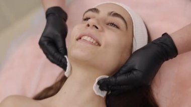 Hidratlaştırıcı yüz bakımı, ferahlatıcı tedaviler, estetikçi tavsiyeleri. Yüz uzmanı yüzü nemlendirmek için pamuk pedleri kullanır..