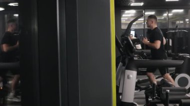 Kalori yanığı, koşu ayakkabısı, spor takip cihazı. Genç adam spor salonunda koşu bandı kullanarak formda kalıyor..