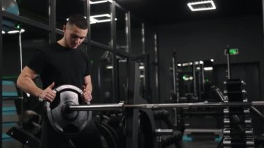Halter egzersizi, fitness golleri, kas tonlaması. Adam spor salonunda ağırlık ekleyerek halterini hazırlıyor..
