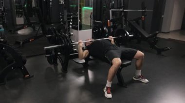 Profesyonel atlet, Bench Press, Hardcore Spor Salonu. Vücut geliştirici, kollarını hedef almak için ağırlık makineleri kullanıyor ve ayrıca halter banklarına odaklanıyor..