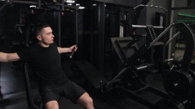 Güzel egzersiz, göğüs presi, spor salonu motivasyonu. Çekici, yapılı bir adam spor aletlerini kullanarak kolları titizlikle eğitir ve göğüs egzersizlerine odaklanır..