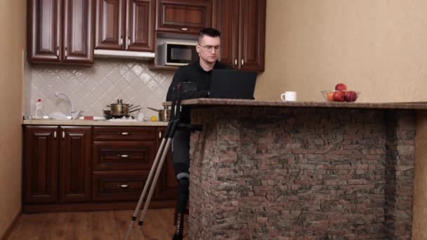 戴眼镜 辅助技术 截肢电脑 带着假肢和眼镜的人在笔记本电脑上工作 拐杖在附近 — 图库视频影像