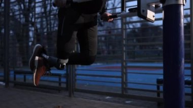 Çekme çubukları, protez bacak, uyarlanabilir fitness. Spor sahasında düzensiz barfiks çekerek protez bacak egzersizi yapan engelli bir adam..