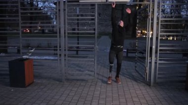 Spor meraklısı, protez bacak, fiziksel aktivite. Protez bacaklı spor meraklısı akşamları fiziksel aktivitelere katılıyor ve spor sahasında barfiks çekiyor..