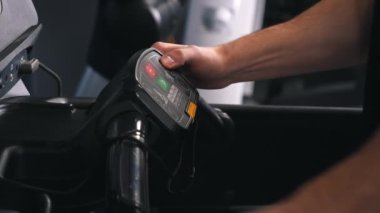 Kontrol arayüzü, hız ayarlama, fitness ekipmanları. Koşu bandındaki düğmelere basan insanların elleri görülebilir..