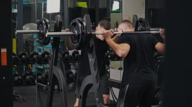 Halter egzersizleri, spor salonu motivasyonu, sağlıklı yaşam tarzı. Vücut geliştiren güçlü erkeksi enerji, vücut geliştirici, sağlık ve sağlığa bağlılığın bir göstergesi olarak boyunlarında ağırlıklarla halter çömelmeleri yürütür..