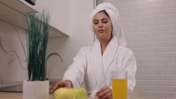 嬉闹的抛掷 微笑的女性 健康的习惯 身着浴衣的年轻女子站在厨房里 一边欢快地在空气中翻滚着绿色的苹果 一边提倡健康的营养和素食的生活方式 — 图库视频影像