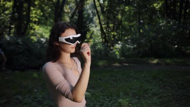 Bulanık bir doğa arka planında, gün batımında VR gözlüklü genç bir kadın tarafından insanlarla ve teknolojiyle dolu bir parkta açık hava oyunu oynanıyor.