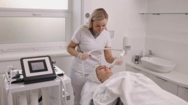 Cilt bakımı, Gençleştirme Susuzluğu, Lenfatik drenaj. Genç bir kadın güzellik elektroporasyon cihazları yardımıyla yüz kaslarına masaj yaptırıyor. Kadın elektrikli yüz bakımı yaptırıyor.