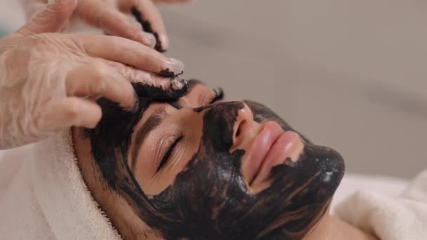 ケルプ若返り クレンジングトリートメント マウスマスク 美容室美容師は 顔のデトックス リフティング 藻類の若返り 泥の治療 にきびケアを提供し 患者の顔に黒いマスクを置きます — ストック動画