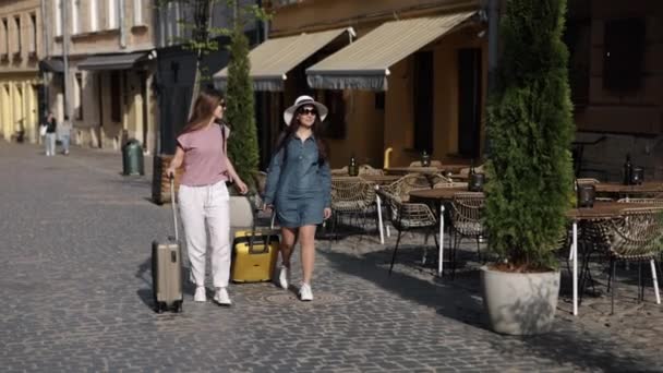 一起旅行 女性朋友 微笑年轻 两个漂亮的女旅行家背着手提箱在城市街道上散步 享受着她们的海外旅行 — 图库视频影像