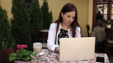 Serbest Çevrimiçi, pozitif öğrenci, dizüstü bilgisayar. Serbest çalışan bir kadın, dışarıda, kafede dizüstü bilgisayarıyla çalışıyor..
