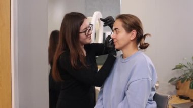 Kaş kaplaması, yüz bakımı, güzellik salonu. Bir güzellik salonunda kaşları düzeltilmiş genç bir kadın, mikro patinaj konsepti boya ile kaşlarını boyuyor.