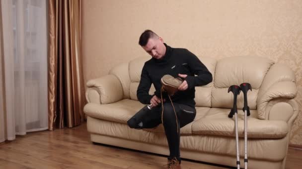 沙发坐 鞋子放进去 有假腿和残疾的男人坐在沙发上穿鞋 他的拐杖就在附近 — 图库视频影像