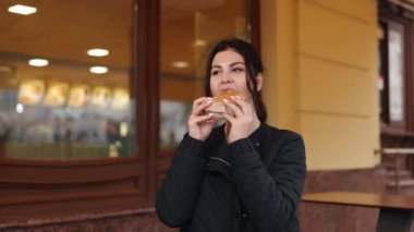 Kadın açık havada, veranda yemeği, restoran civarında. Restoranın dışında, genç esmer kadın hamburger yiyor..