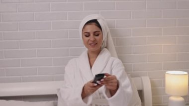 Televizyon programlama, ev eğlencesi, dijital navigasyon. Bornoz giymiş bir kadın uzaktan kumandayla yatak odasındaki televizyon programlarını seçiyor..