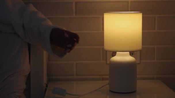 ハンドスイッチ ライト調整 女性の手 女性の手はランプをオフに切り替えます 明るいベッドルーム — ストック動画