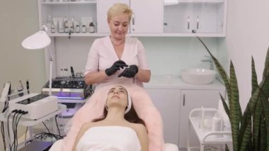Kadın kozmetik uzmanı, masaj teknikleri, cilt hidrasyonu. Kadın kozmetolog müşterilerin yüzüne krem sürer ve canlandırıcı masaj uygular..