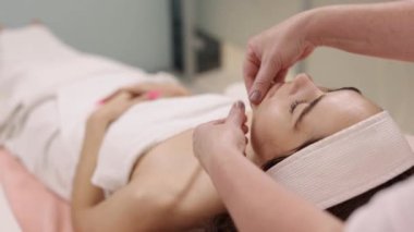 Rahatlatıcı masaj, canlandırıcı terapi, cilt yenileme. Kadın kozmetik uzmanı, yüz masajını canlandırırken müşterilerin yüzüne krem sürüyor..