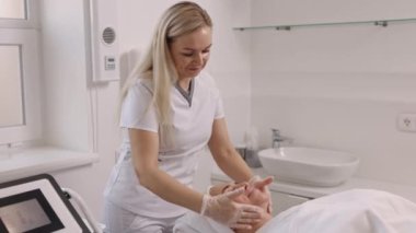 Güzellik kliniği, yüz masajı, yüz bakımı. Güzellik kliniğinde yüz masajı yaptıran güzel bir kadın, sırt üstü uzanan genç bir kadın, yüz masajı yaptıran, kafa havlusu, cilt bakımı, kaplıca konsepti.