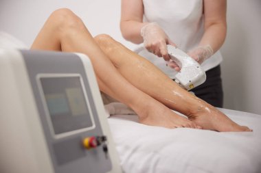 Kadınların bacakları, kozmetoloji prosedürleri, doktorların elleri. Kadınların bacaklarında lazer ameliyatı, güzellik salonunda lazer epilasyon ve kozmetoloji, saç çıkarma kozmetoloji prosedürü, lazer epilasyon.