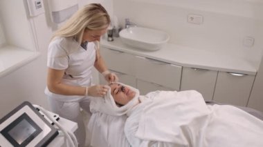 Cilt bakımı uzmanı, Holistik tedaviler, cilt temizleme. Güzellik salonundaki müşteriler yüz yüzeyine cilt bakımı uzmanları tarafından uygulanan siyah maske tedavisi görüyorlar.,