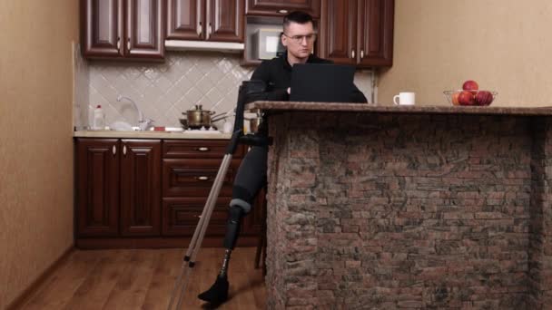 ノートパソコンの仕事障害者支援足の切断 眼鏡をかけノートパソコンで手に松葉杖を持つ男 — ストック動画
