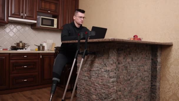 人工手足ノートパソコン作業支援ソリューション 義足の男と眼鏡はラップトップで動作します 近くの松葉杖 — ストック動画