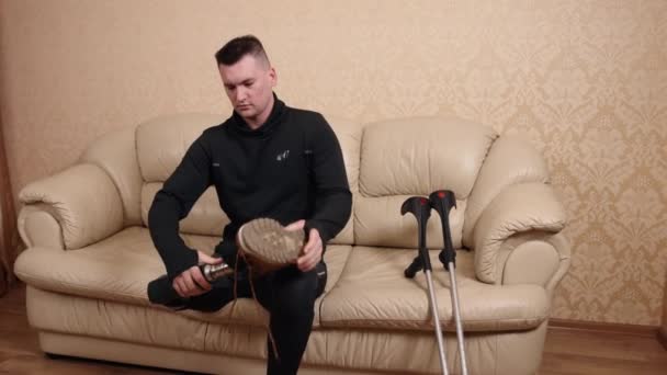 拐杖休息 身体损伤 残疾技术 假腿的人穿上鞋子 坐在沙发上 手握拐杖 因为他有残疾 — 图库视频影像