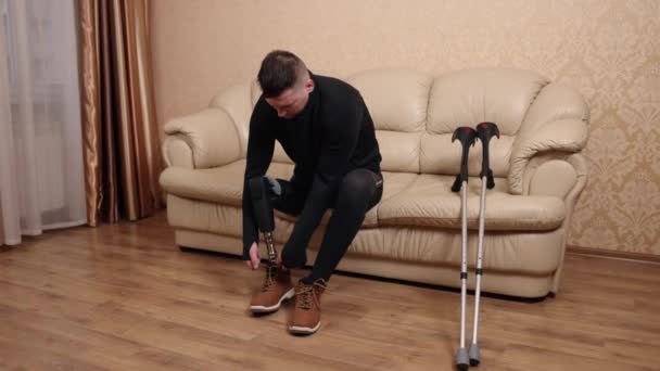福祉機器靴の装着障害技術 足が不自由で義足の男がソファに座りながら靴を履いている — ストック動画