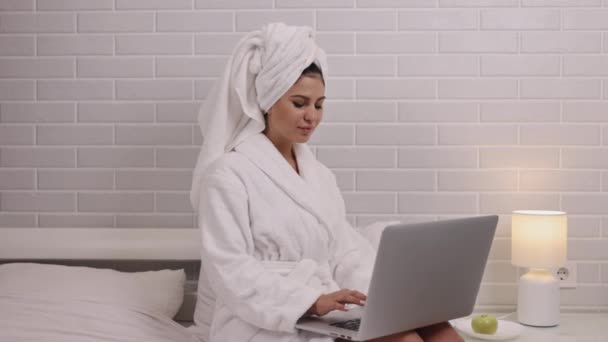 ラップトップ 女性のフリーランス ベッドルームの生産性を使用しています ベッドルームに座り バスローブを着て 女性はノートパソコンで仕事に従事しています — ストック動画