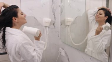 Evde, duşta, sabah saç kurutma makinesinde. Sabah duşundan sonra kadın saç kurutma makinesini ev banyosunda saç kurutmak için kullanıyor..