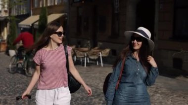 Çanta taşıma, yaz tatili, turist seyahati. İki güzel kadın, turistler, caddeden aşağı iniyorlar, bavulları kendilerine eşlik ediyor, yabancı topraklarda yolculuklarının tadını çıkarıyorlar..
