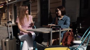 İki gezgin, oturanlar, telefon aktiviteleri. İki kadın turist, ellerinde telefonlarıyla, bavullarıyla masada bekliyorlar..