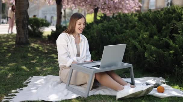 视频通话 视频会议 公园会议 这个女人把自己安置在外面的树下 通过笔记本电脑参加视频会议 — 图库视频影像