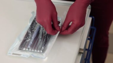 Sterile instruments, Dentist hygiene, Sterilization process. Close-up of dentists hands methodically unwrapping sterile instruments for oral examination.