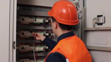 Elektriksel, elektrikçi ölçümleri, güvenlik kontrolleri yapıyor. Fabrikada, kontrol panelindeki akım çoklu metre kullanan elektrikçiler tarafından ölçülür..