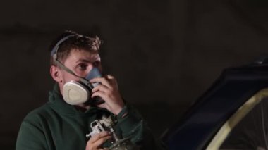 Güvenlik önlemleri, güvenlik prosedürleri, güvenlik yönergeleri. Adam araba boyama görevine hazırlanırken gaz maskesi takıyor..