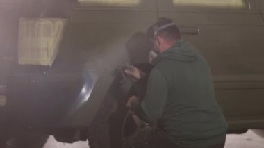 Boya malzemeleri, boya koruması, boya uygulaması. Solunum cihazına bağlanmış bir adam sprey tabancayla arabaya boya sürüyor..