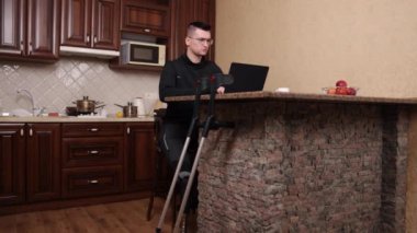 Bozuk destek, protez bacak, gözlük. Protez bacaklı, gözlüklü, laptopta koltuk değnekleriyle çalışan bir adam..